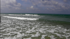 The image shows a seascape with waves crashing onto the shore under a cloudy sky.