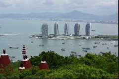 Here's a description of the image:A scenic view of Sanya, China, featuring unique hotel towers along the coastline, dotted with boats in the bay, captured from an elevated perspective with traditional structures in the foreground.