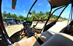 The view from inside a helicopter on a sandy beach, with palm trees visible outside through the open doors.