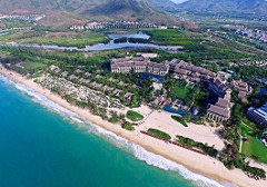An aerial view captures a luxurious coastal resort with its structures nestled between a pristine beach and verdant landscape.