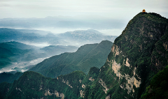 A majestic mountain range with a golden temple atop one peak, shrouded in mist and greenery.