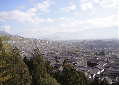 A panoramic view of a dense cityscape with traditional tiled roofs stretching across the landscape towards distant mountains under a bright sky.