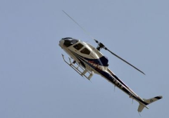 A white and blue helicopter is flying in the clear blue sky.