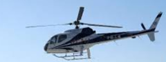 A white and blue police helicopter flies against a clear blue sky.