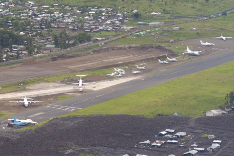 Aerial view of Goma International Airport in the Democratic Republic of Congo, showcasing various aircraft on the runway and apron amidst lush greenery and urban development.