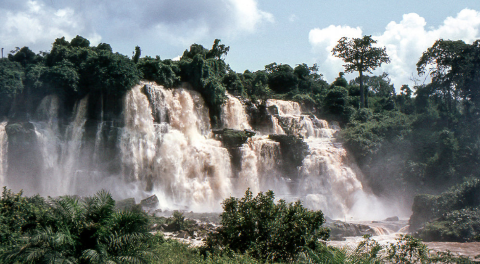 The image depicts a cascading waterfall in a lush, green environment under a partly cloudy sky.