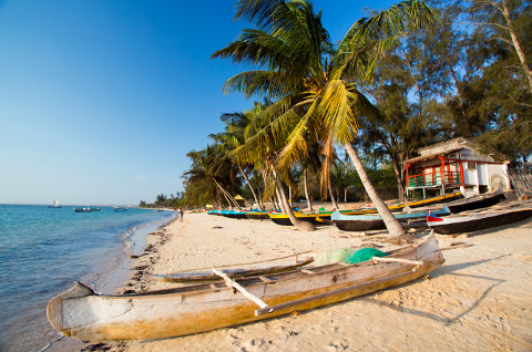 A sunny beach scene in Madagascar with canoes on the sand near palm trees and a small white house.