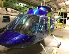 Cali Helicopter Tour - Best Value Aerial Tour - Best Pilots A blue and green helicopter sits in a hangar next to another helicopter and a yellow rolling platform.