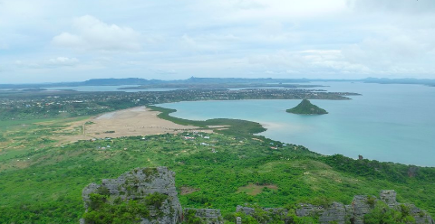 A scenic landscape view from atop Montagne des Français in Diego Suarez, showcasing a coastal town, a large bay with an island, and lush green vegetation.