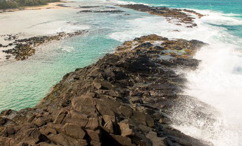 A scenic shot captures waves crashing against a rocky shoreline with light blue water.