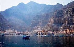 A scenic view of a coastal town nestled against towering mountains, with a tranquil bay dotted with boats.