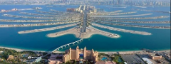 Aerial view of the Palm Jumeirah in Dubai, an artificial archipelago resembling a palm tree, with the Atlantis hotel in the foreground and city skyline in the background.