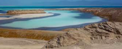 This image showcases a landscape with a turquoise lagoon surrounded by arid, rocky terrain, leading to a blue sea in the distance.