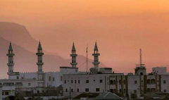 Uma paisagem urbana de edifícios brancos e minaretes sob um céu alaranjado e nebuloso na Somália, com montanhas ao fundo.