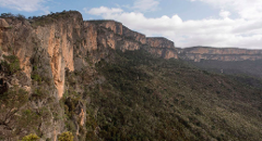 Uma vista panorâmica de uma paisagem montanhosa na Somália, com penhascos rochosos e vegetação densa sob um céu parcialmente nublado.