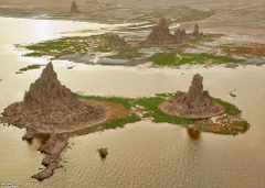 An aerial shot shows rocky, spire-like formations rising from islands in a calm body of water, hinting at a unique landscape.