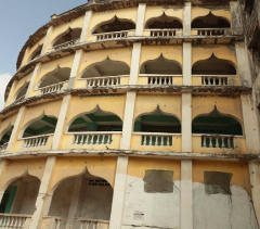 Here's a description of the image:A multi-story, curved building with arched openings and balconies, showing signs of age and neglect in Mogadishu, Somalia.