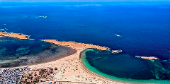 Uma vista aérea de Kismayo, Somália, mostra uma península conectada ao continente por um banco de areia, com assentamentos e mar azul ao fundo.