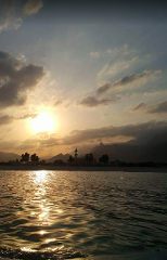 A serene sunset bathes the Puntland coastline, with a mosque silhouette and rolling hills in the distance, reflected in the gently rippling waters.