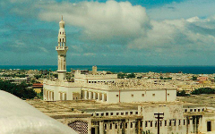 The image shows the Islamic Solidarity Mosque in Mogadishu, Somalia, with its tall minaret standing out against the cityscape and the sky.