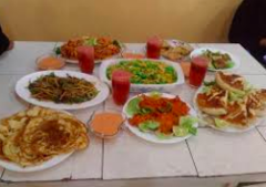 A table laden with various Somali dishes, including rice, pancakes, salads, and fried foods, along with glasses of a reddish drink, suggesting a communal meal or feast.