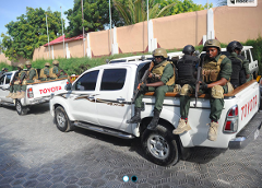 Two white Toyota trucks carry armed personnel in military gear, likely patrolling or responding to a security situation.