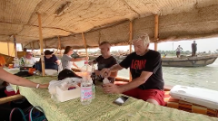 People are gathered on a boat with a thatched roof, sharing drinks and enjoying the scenery.