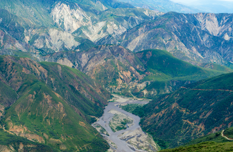 A breathtaking aerial view of a winding river carving through a mountainous landscape, with layers of green and gray peaks stretching to the horizon.