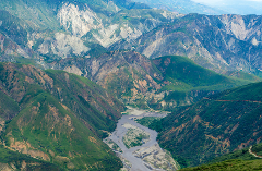 A breathtaking aerial view of a winding river carving through a mountainous landscape, with layers of green and gray peaks stretching to the horizon.