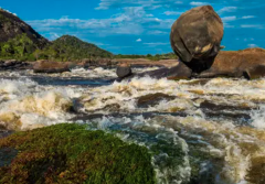 El Tuparro National Park - 5 Days A river flows rapidly through rocky terrain, with a large, rounded rock precariously perched on top of another rock formation.