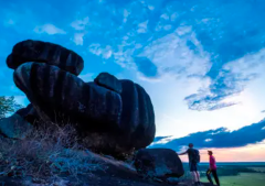 El Tuparro National Park - 5 Days Two people stand near large rock formations under a partly cloudy, blue sky at dusk.