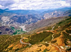 A high-angle landscape shot of a winding road cutting through mountainous terrain with a village nestled in the valley below.