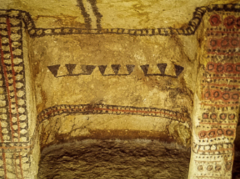 This image shows a part of an ancient cave painting with geometric patterns and symbols in dark brown and red colors on a light yellow-brown background.