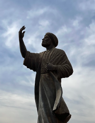 En bronzestatue af en mand iført turban og kåbe med den ene arm hævet mod himlen.