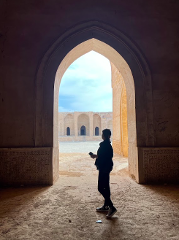 A person stands in a large arched doorway of a building, looking out at a courtyard.