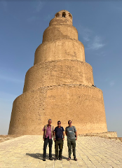 Three men pose in front of the Great Mosque of Samarra's spiral minaret under a clear, sunny sky.
