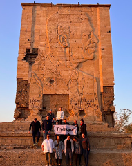 A group of people posing in front of a large stone structure with a carved portrait of a man, holding a "Trekup" banner.