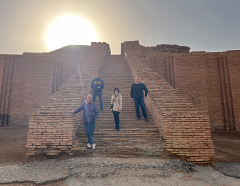 Four people stand on the brick steps of a large ziggurat-like structure, illuminated by the sun.