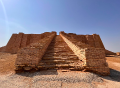 A ziggurat in Iraq with long stairs leading up to the top, under a clear blue sky.