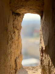 A close-up shot captures a view through a rough-hewn stone window, revealing a blurred landscape bathed in soft, diffused daylight.