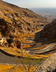 A winding road snakes through a dry, mountainous landscape under a hazy sky.