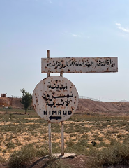 Ein rostiges, verwittertes Schild weist den Weg zur archäologischen Stätte Nimrud, mit arabischem Text über der englischen Übersetzung.