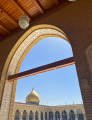 A view through an ornate archway captures a golden dome and courtyard under a clear sky.