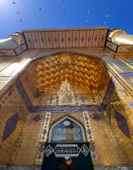 A low-angle shot of an ornate golden archway with detailed Islamic calligraphy and geometric patterns, featuring a chandelier and decorative elements.
