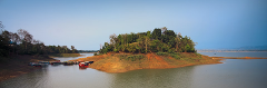 A scenic view of an island covered in lush greenery surrounded by water, with several boats docked on one side, under a clear blue sky.