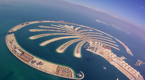 An aerial view captures the man-made Palm Jumeirah island in Dubai, featuring a palm tree design with a crescent surrounding it, set against the backdrop of the sea and sky.