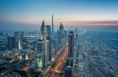 An aerial view of Dubai's skyline at dusk with the Burj Khalifa dominating the cityscape and illuminated highways stretching into the distance.