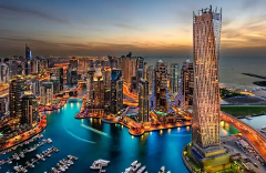This is a vibrant, panoramic view of Dubai Marina at dusk, showcasing its modern skyscrapers, illuminated waterways filled with boats, and a captivating sunset backdrop.