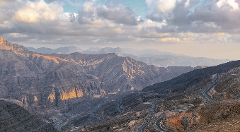 A scenic view of mountains with a winding road under a cloudy sky.