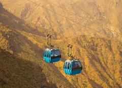 Two blue cable cars hang suspended in mid-air, traversing a mountainous landscape.